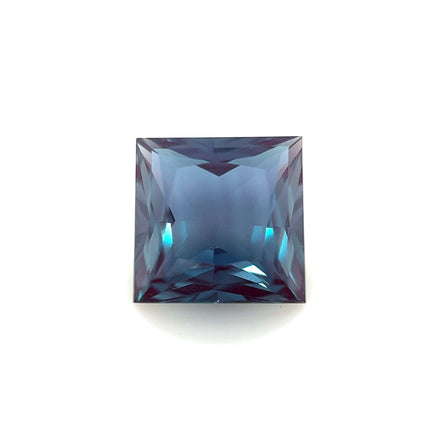 The 8mm Exceptional Square Princess Lab Created Alexandrite, a square-cut gemstone with a deep blue hue and sharp facets, is displayed against a plain white background.
