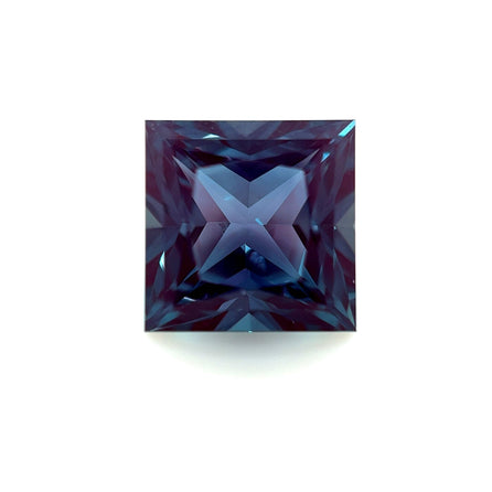 The 9mm Exceptional Square Princess Lab Created Alexandrite shows deep blue and purple hues, with intricate faceting that forms an X-shaped reflection at its center, displayed against a white background.