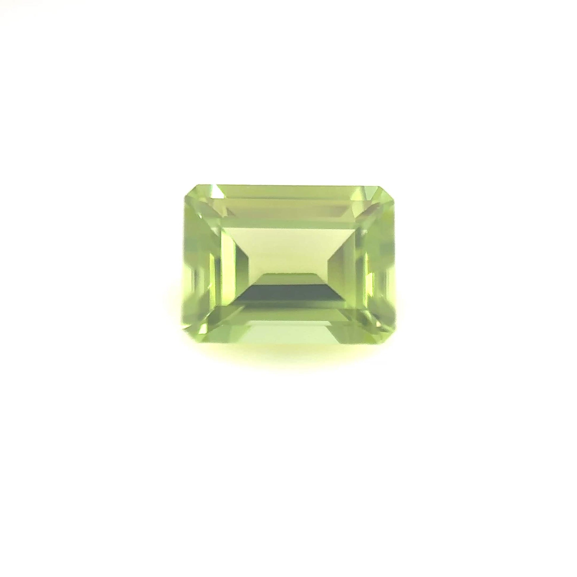 The 8.0x6.0 Premium Emerald Peridot features a natural rectangular cut with sharp facets, displayed against a plain white background.