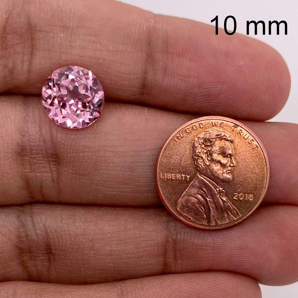 A 10.00-10.00 mm Premium Round Padparadscha and a 2018 U.S. penny rest on a hand, with the penny highlighting the size of this beautiful gemstone for easy comparison.