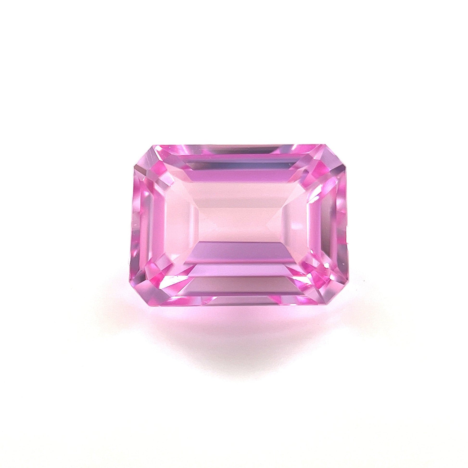 An 8.0x6.0 Exceptional Emerald Lab Created Medium Pink Sapphire with beveled edges is displayed on a white background, reflecting light and showcasing medium pink hues with intricate facets.