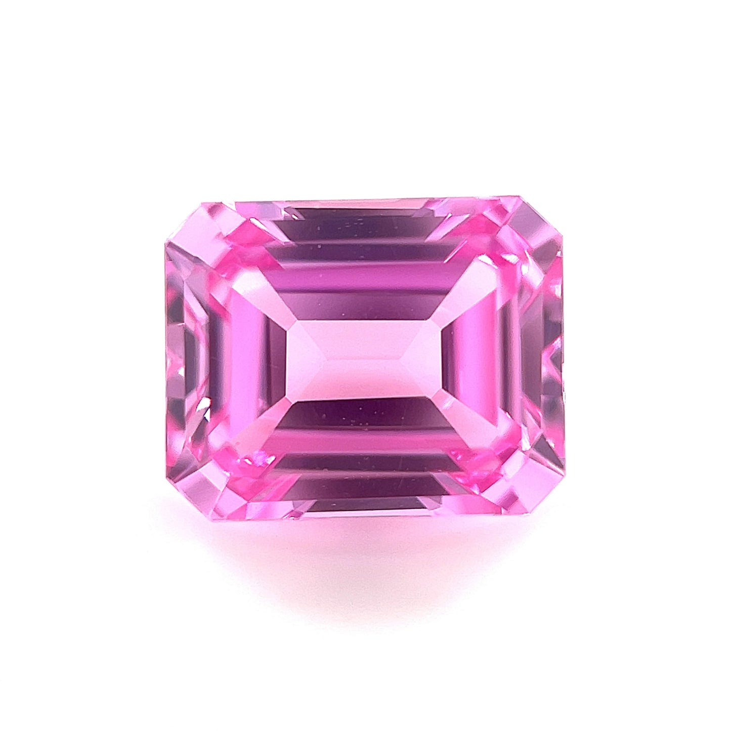 The 10x8 Exceptional Emerald Lab Created Medium Pink Sapphire features sharp facets and a bright, reflective surface, displayed from above on a white background.