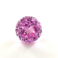 A 10mm Exceptional Round Lab Created Medium Pink Sapphire with a sparkling, faceted surface is displayed against a plain white background.