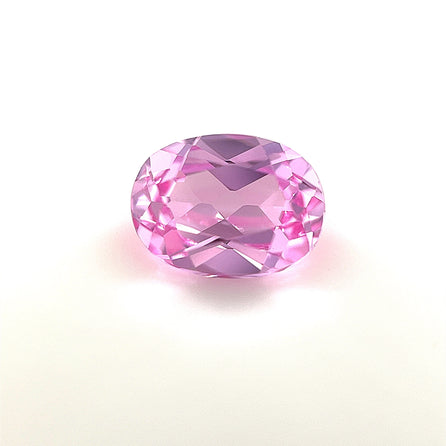 An 8x6 Exceptional Oval Lab Created Medium Pink Sapphire is displayed on a white background, highlighting its sparkling faceted cut and clarity.