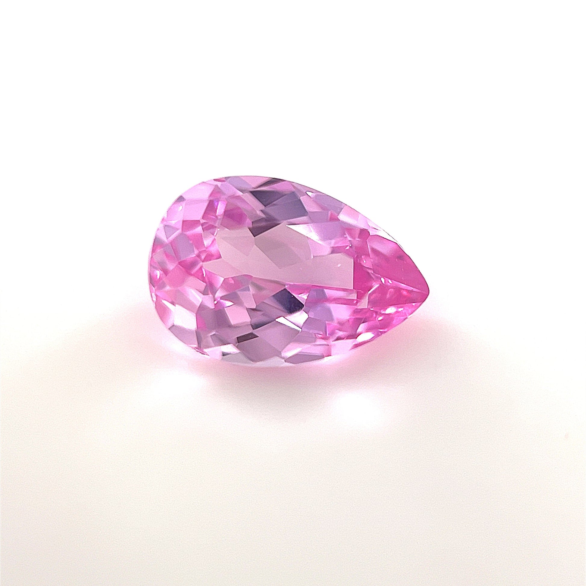 A 9x6 Exceptional Pear Lab Created Medium Pink Sapphire with a faceted surface is shown on a plain white background, highlighting its brilliant reflectivity and vibrant medium pink hue.
