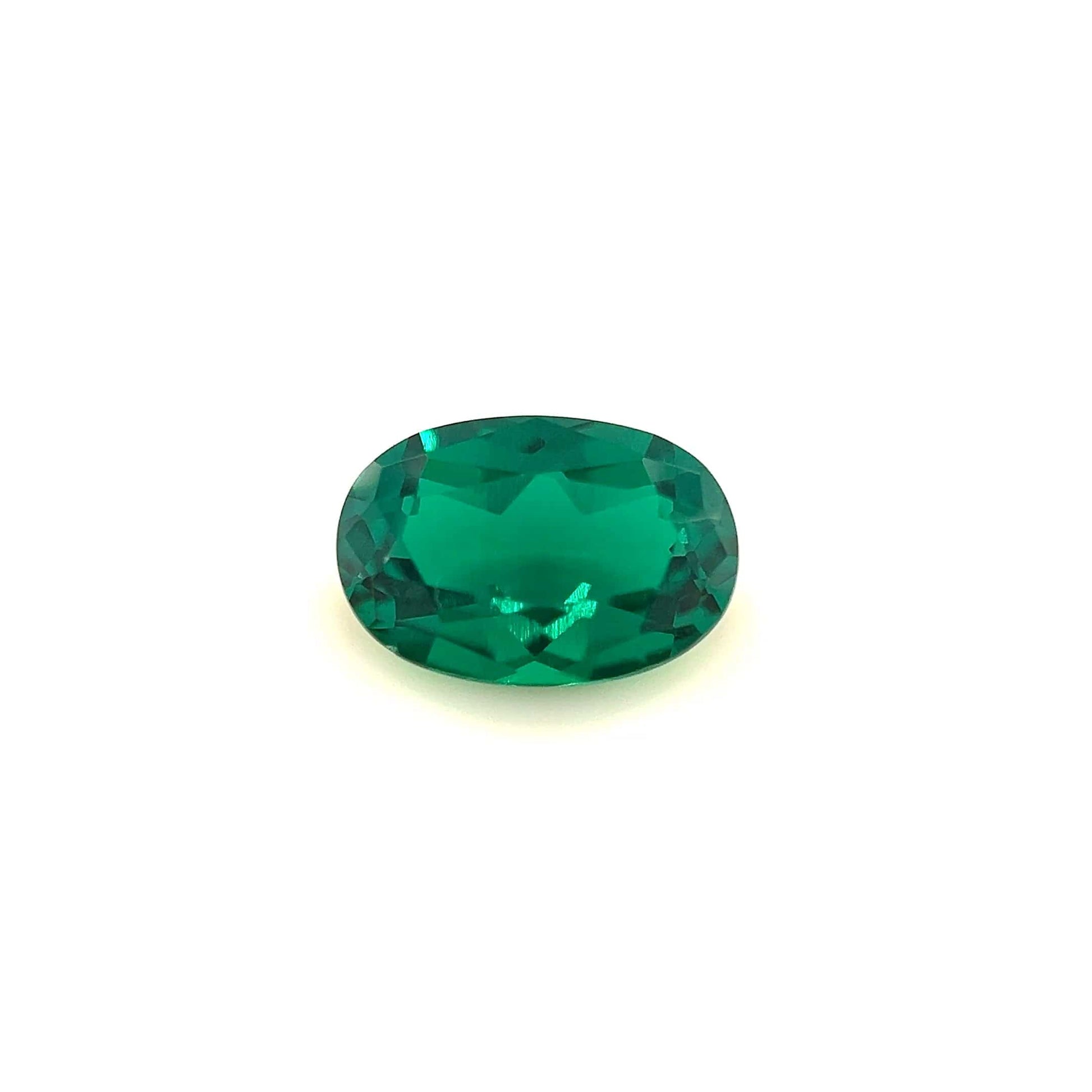 The 9.0x6.0 Exceptional Oval Zambian Color Lab Created Emerald features a faceted, vivid green stone that glows brightly against a plain white background.