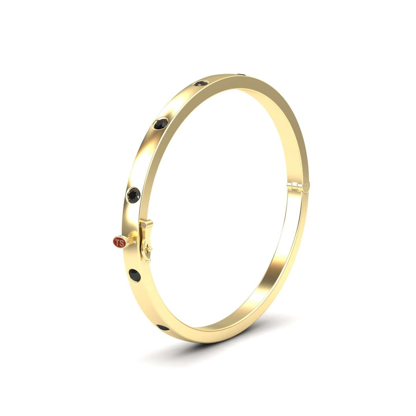 The Black Diamond Bezel-Set Bracelet - Flavia is a gold bangle featuring evenly spaced black diamond accents and a small red circular charm on one side, shown against a white background.