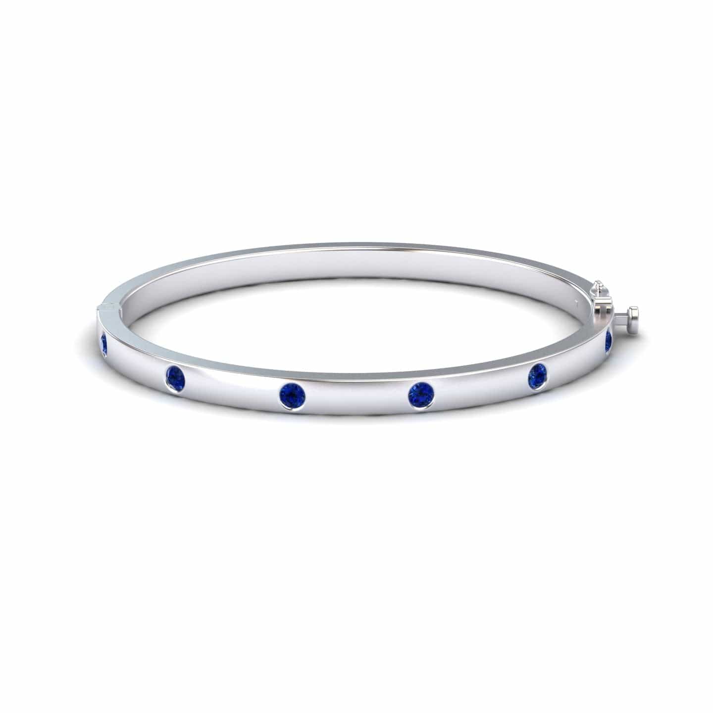 The Blue Sapphire Bezel-Set Bracelet - Flavia features a silver bangle adorned with evenly spaced round blue sapphires, showcased on a white background.
