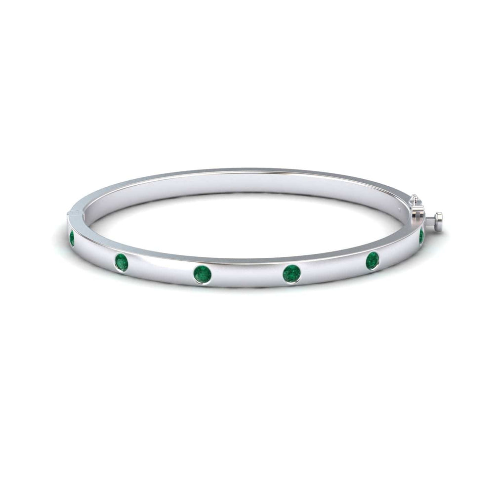 The Emerald Bezel-Set Bracelet - Flavia is a silver bangle adorned with evenly spaced round green gemstones, shown on a white background.