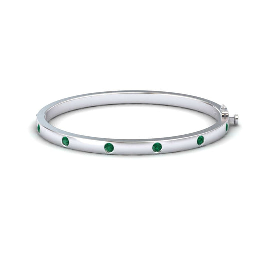 The Emerald Bezel-Set Bracelet - Flavia is a silver bangle adorned with evenly spaced round green gemstones, shown on a white background.