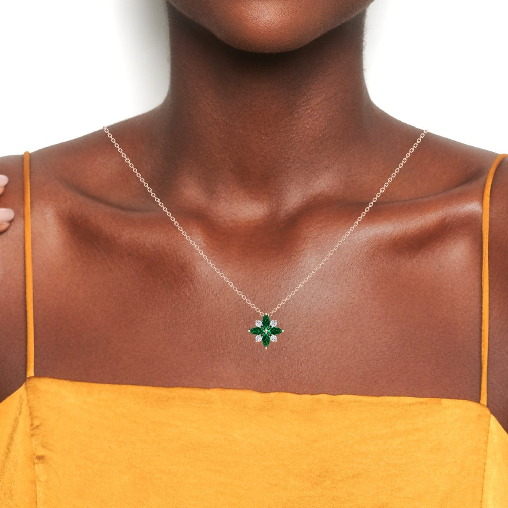A person in a yellow top showcases the Emerald & Diamond Flower Necklace - Keira, featuring a delicate silver chain with a green gemstone flower pendant, against a white background.