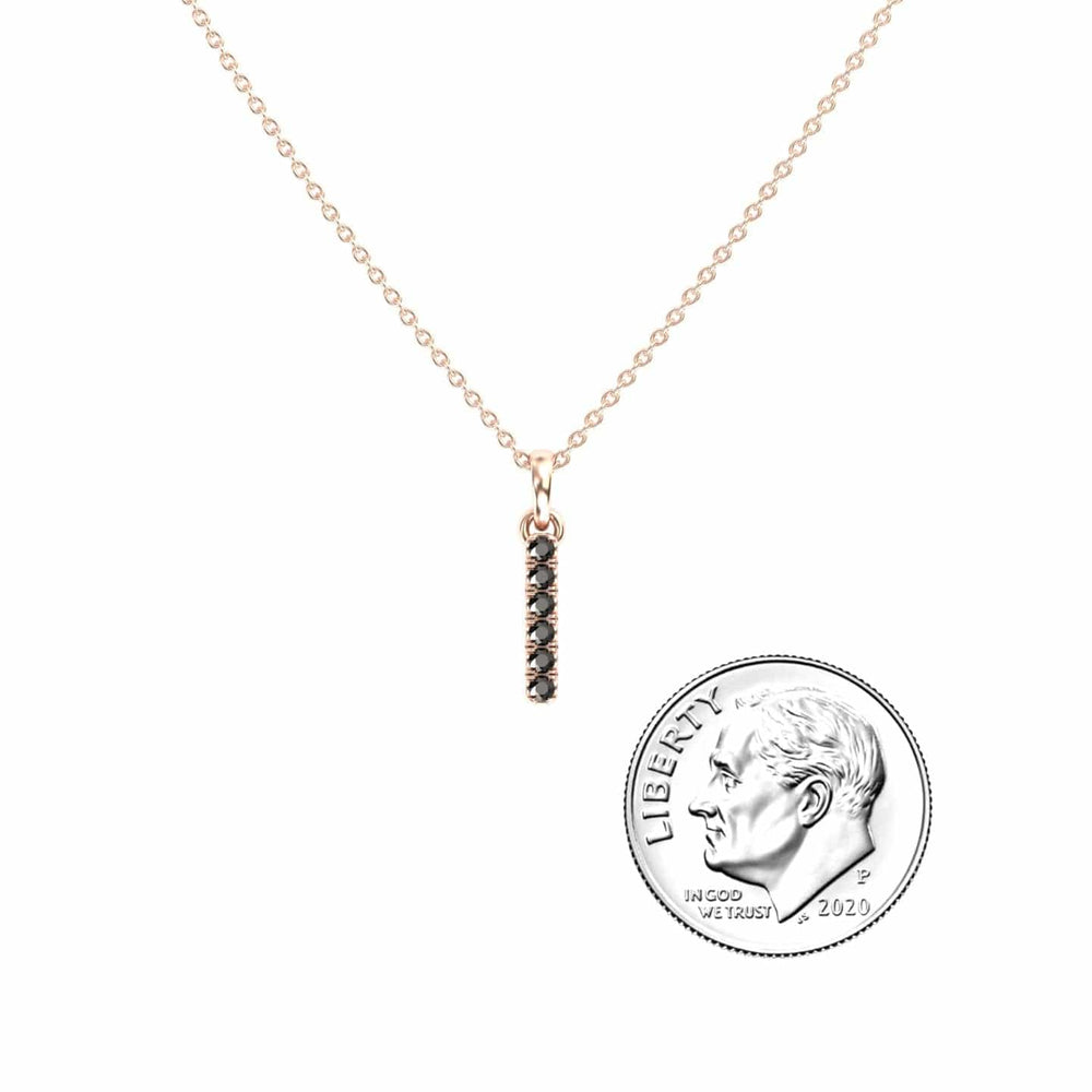 The Black Diamond Vertical Bar Necklace - Lalita features a delicate gold chain and a pendant with small black stones, shown next to a U.S. dime for size reference.