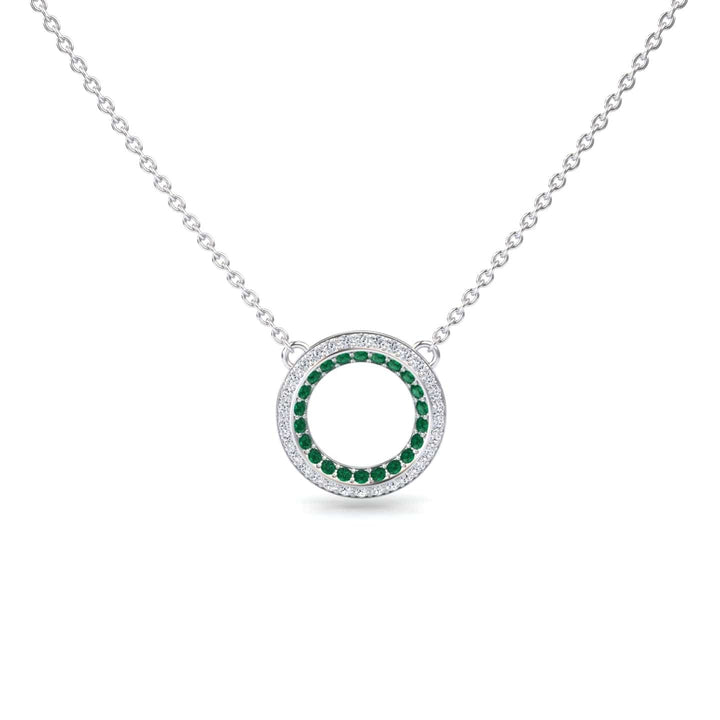 The Emerald & Diamond Double Halo Circle Necklace - Mona features a silver chain with a circular pendant, adorned with a ring of green emeralds encircled by sparkling diamonds.