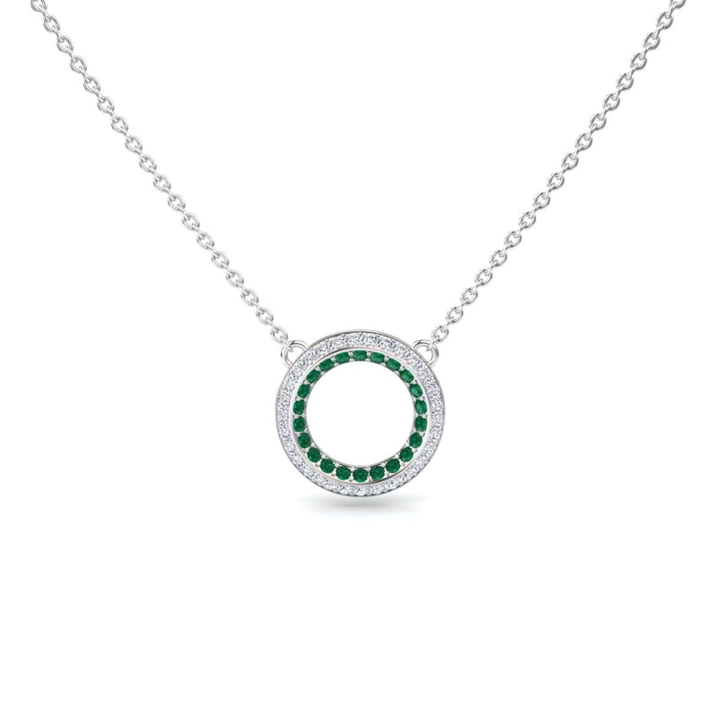 The Emerald & Diamond Double Halo Circle Necklace - Mona features a silver chain with a circular pendant, adorned with a ring of green emeralds encircled by sparkling diamonds.
