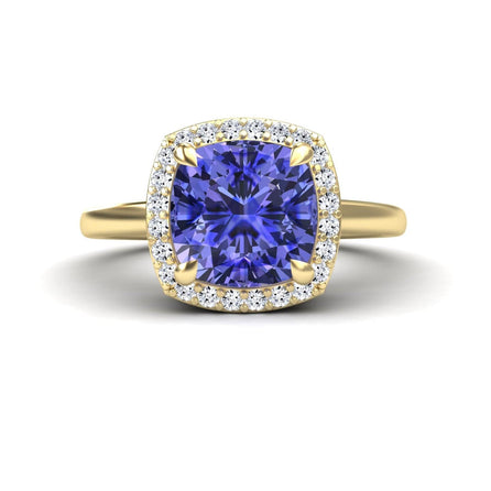 The Ziva Tanzanite & Diamond Halo Ring showcases a large cushion-cut blue tanzanite at the center, encircled by a halo of small round white diamonds, displayed from the front on a white background.