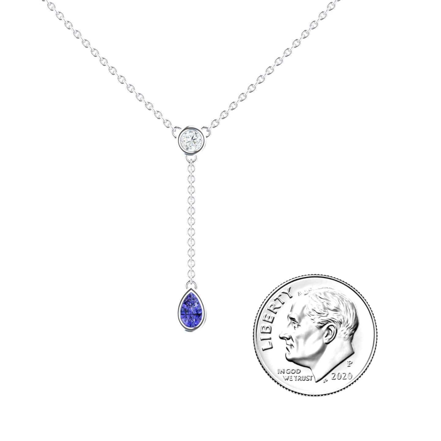 The Tanzanite & Diamond Elegant Drop Necklace - Daniela features a delicate silver chain with a round clear stone and a dangling teardrop-shaped blue gemstone, shown beside a 2020 U.S. dime for scale on a white background.