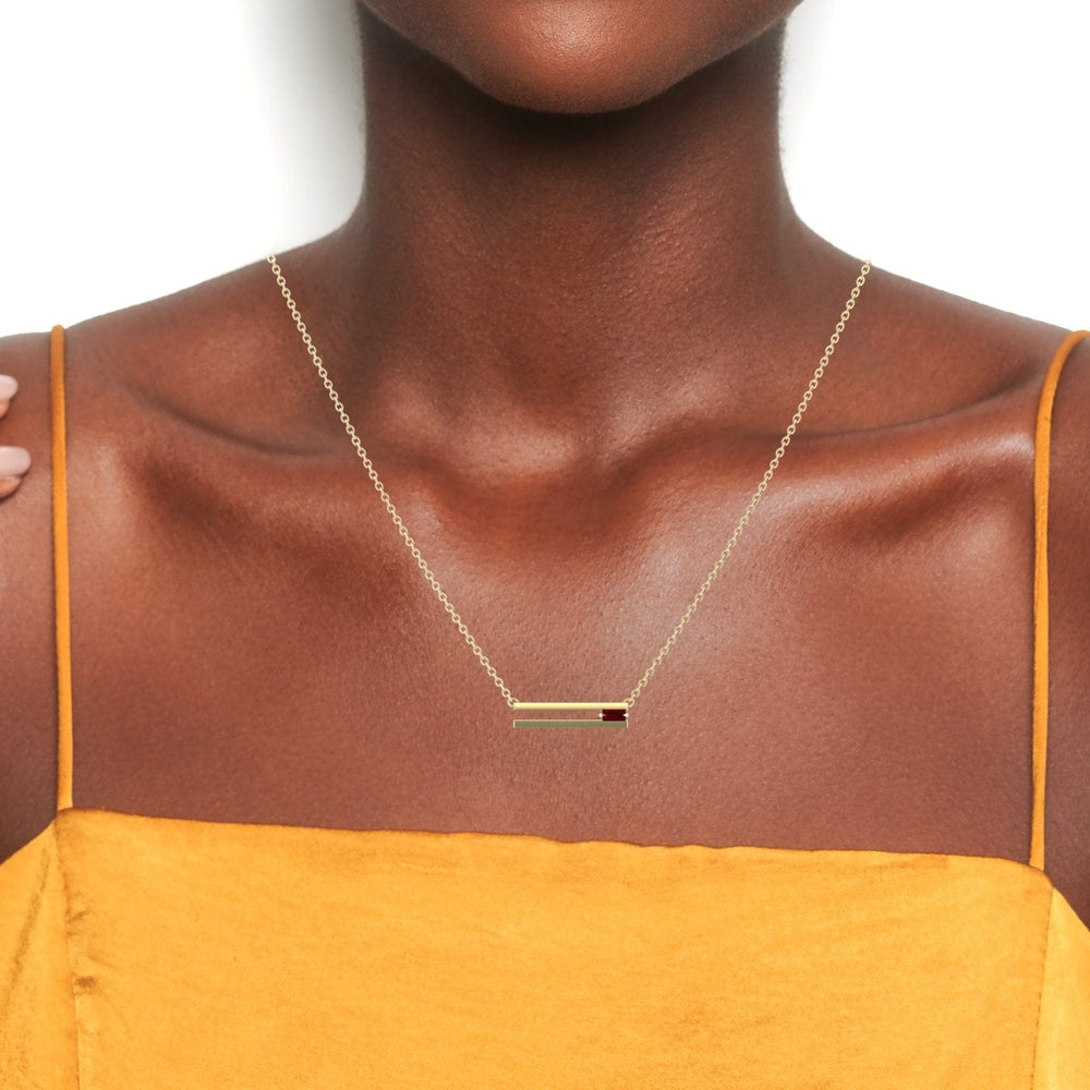 A woman wearing a mustard yellow top and the Garnet Bar Necklace - Cecilia, a delicate gold chain with a horizontal bar pendant, shown from shoulders to chin against a white background.