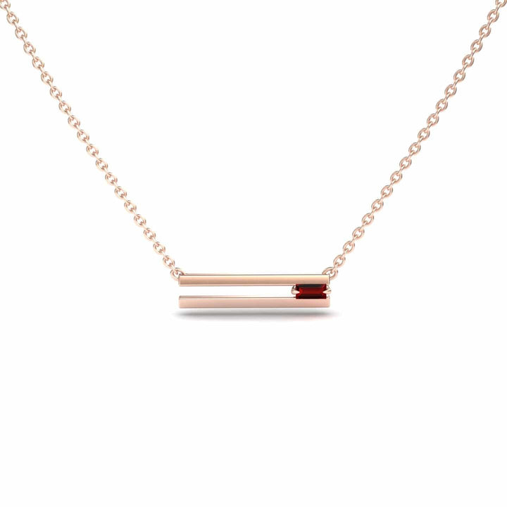The Ruby Bar Necklace - Cecilia is a delicate gold chain with a horizontal bar pendant accented by a small red gemstone on one end, shown against a white background.