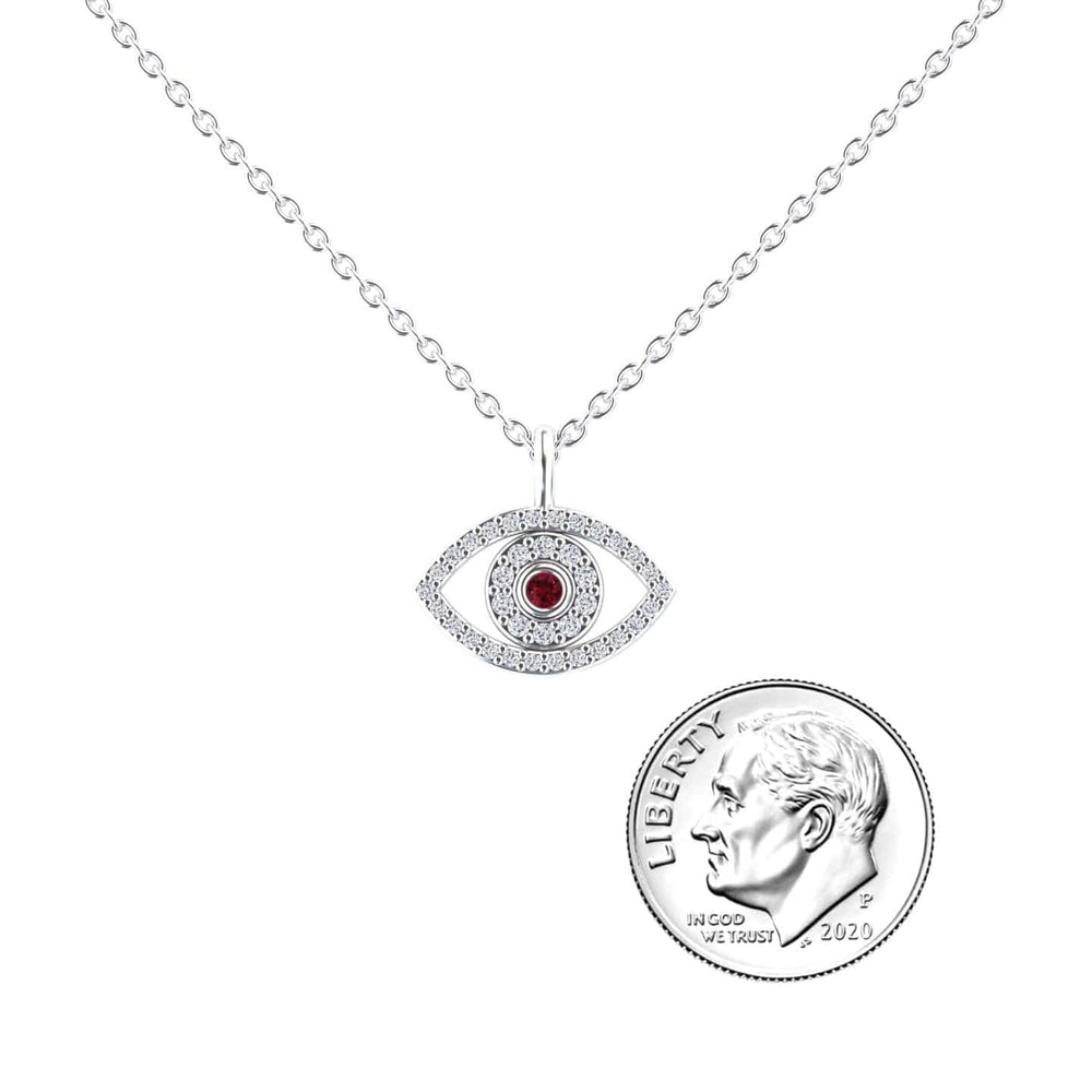 The Ruby & Diamond Eye Necklace - Elise features a silver pendant shaped like an eye with a red center stone, shown beside a U.S. dime for size reference.