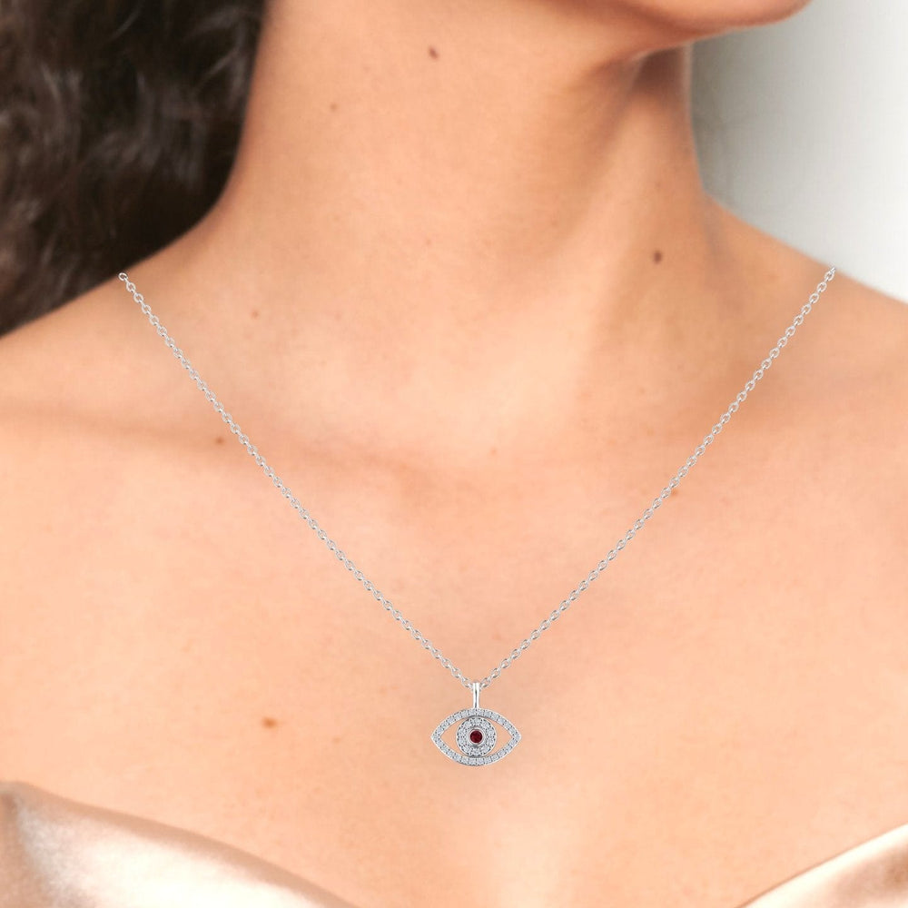 A woman wears the Ruby & Diamond Eye Necklace - Elise, a silver chain with a sparkling eye-shaped pendant and blue center stone, against bare shoulders and a strapless champagne-colored top.