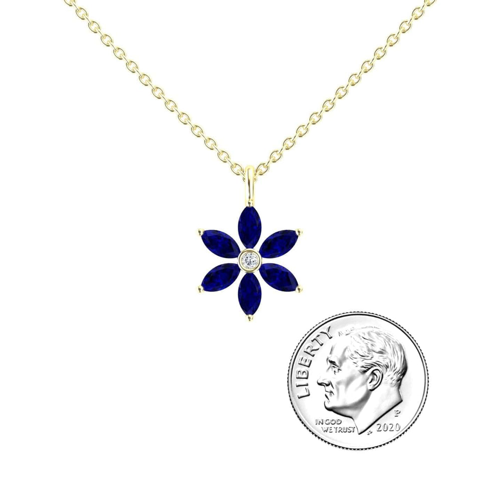 The Lab Grown Blue Sapphire & Diamond Floral Necklace - Erin is shown next to a 2020 U.S. dime for size comparison. The pendant features six blue sapphire petals and a clear diamond center on a gold chain.