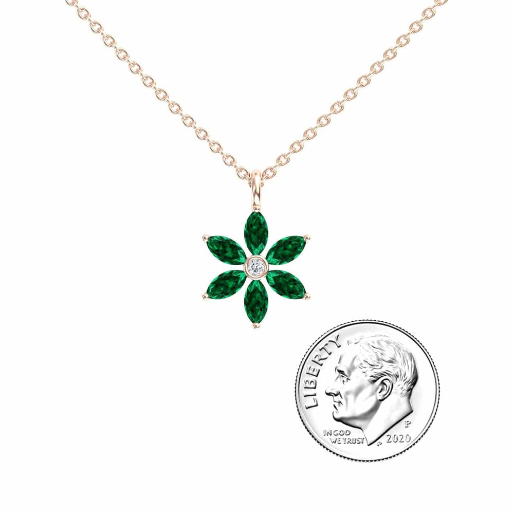 The Lab Grown Emerald & Diamond Floral Necklace - Erin features a gold chain and a flower-shaped pendant with six green stones and a central clear stone, shown beside a 2020 U.S. dime for size comparison.