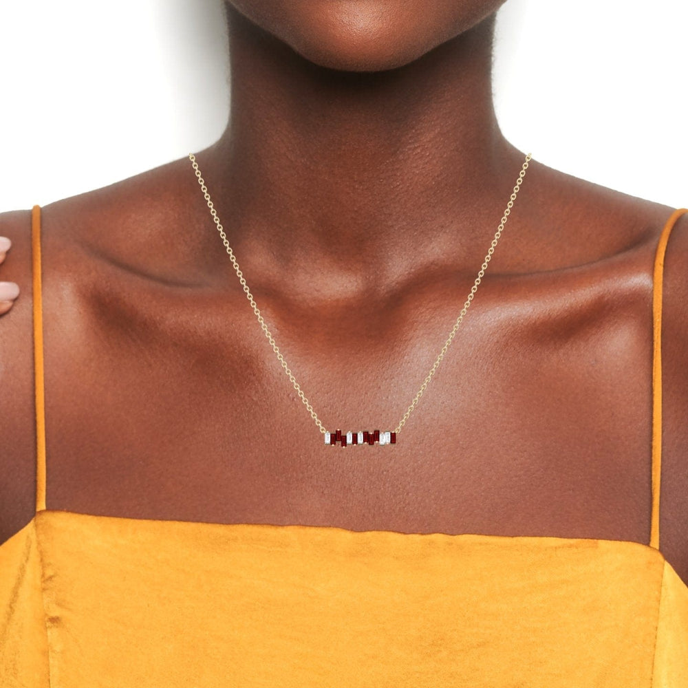 A person wears the Lab Grown Ruby & Diamond Geometric Bar Necklace - Fernanda, featuring rectangular red, white, and maroon beads on a gold chain, paired with a mustard yellow top against a white background.