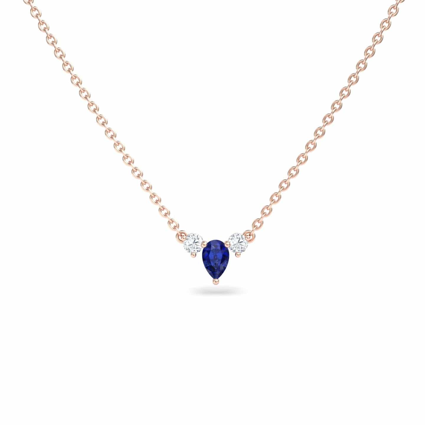 The Blue Sapphire & Diamond Three-Stone Necklace - Jina showcases a teardrop-shaped blue sapphire pendant flanked by two round diamonds, all set on a delicate gold chain against a white background.