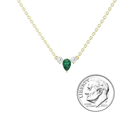 The Emerald & Diamond Three-Stone Necklace - Jina features a delicate gold chain with a teardrop green emerald pendant flanked by two small diamonds, shown beside a US dime for size comparison.