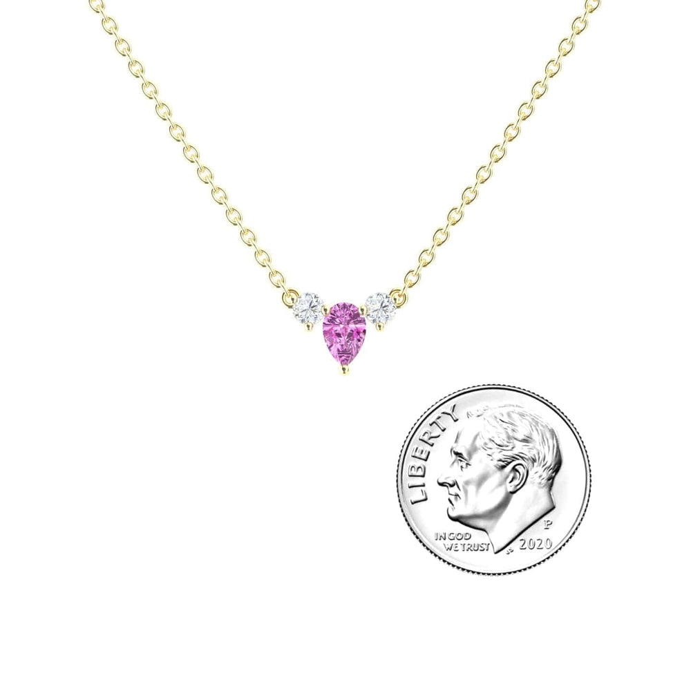 The Pink Sapphire & Diamond Three-Stone Necklace - Jina features a gold chain with a pink sapphire pear center and two small diamonds, shown beside a U.S. dime for size reference.