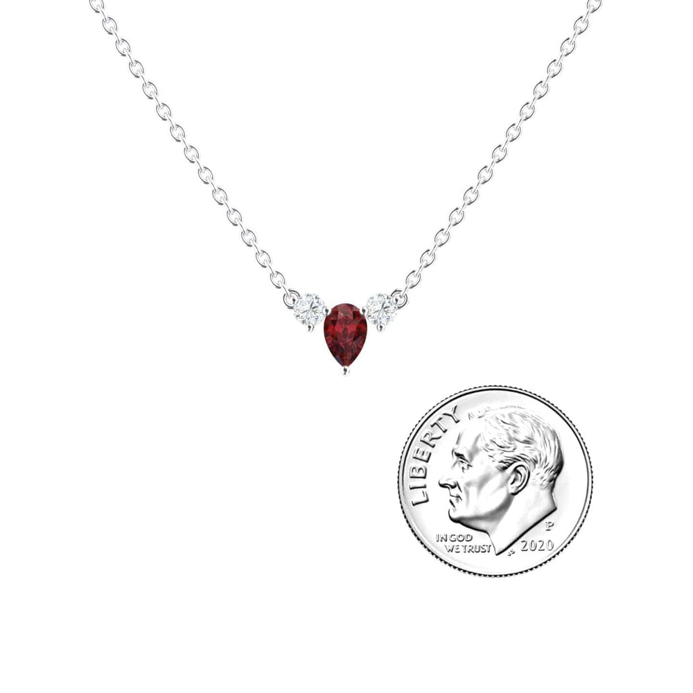 The Ruby & Diamond Three-Stone Necklace - Jina features a red teardrop-shaped ruby pendant flanked by two diamonds on a silver chain, displayed beside a U.S. dime for size reference.