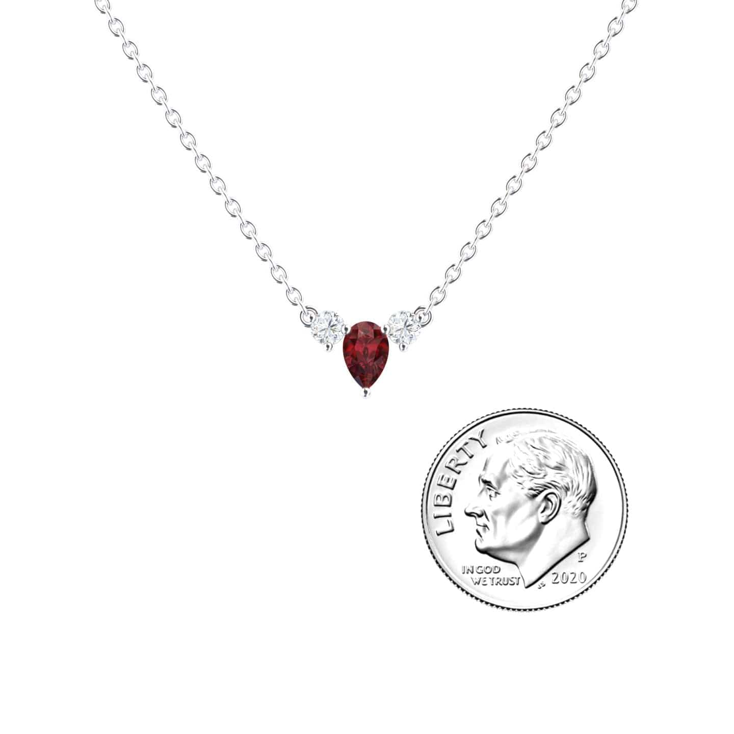 The Ruby & Diamond Three-Stone Necklace - Jina features a red teardrop-shaped ruby pendant flanked by two diamonds on a silver chain, displayed beside a U.S. dime for size reference.