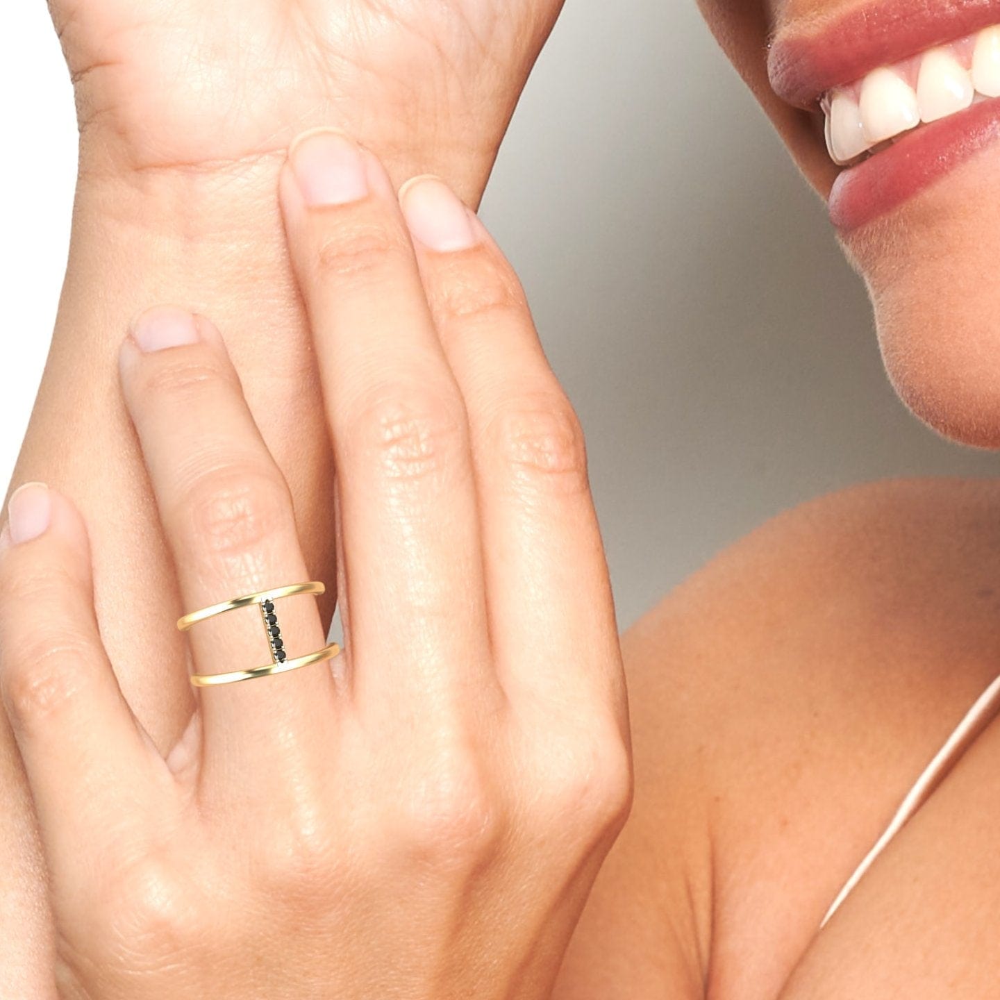 A close-up shows a smiling hand wearing the Black Diamond Vertical Bar Split Band Ring - Opal, featuring a modern gold band with a vertical row of small black stones, set against their cheek and shoulder.