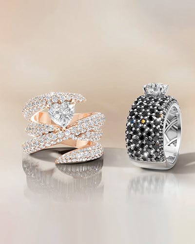 Two elegant rings with intricate designs on a reflective surface.