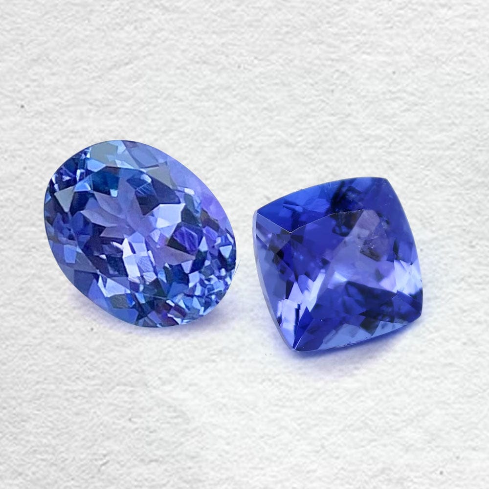 Two blue tanzanite gemstones on a textured white background