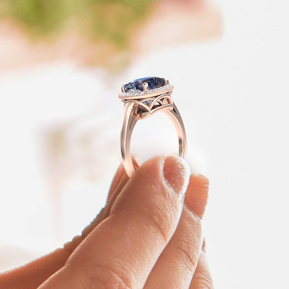 Rose gold ring with a alexandrite gemstone held by a hand against a blurred background