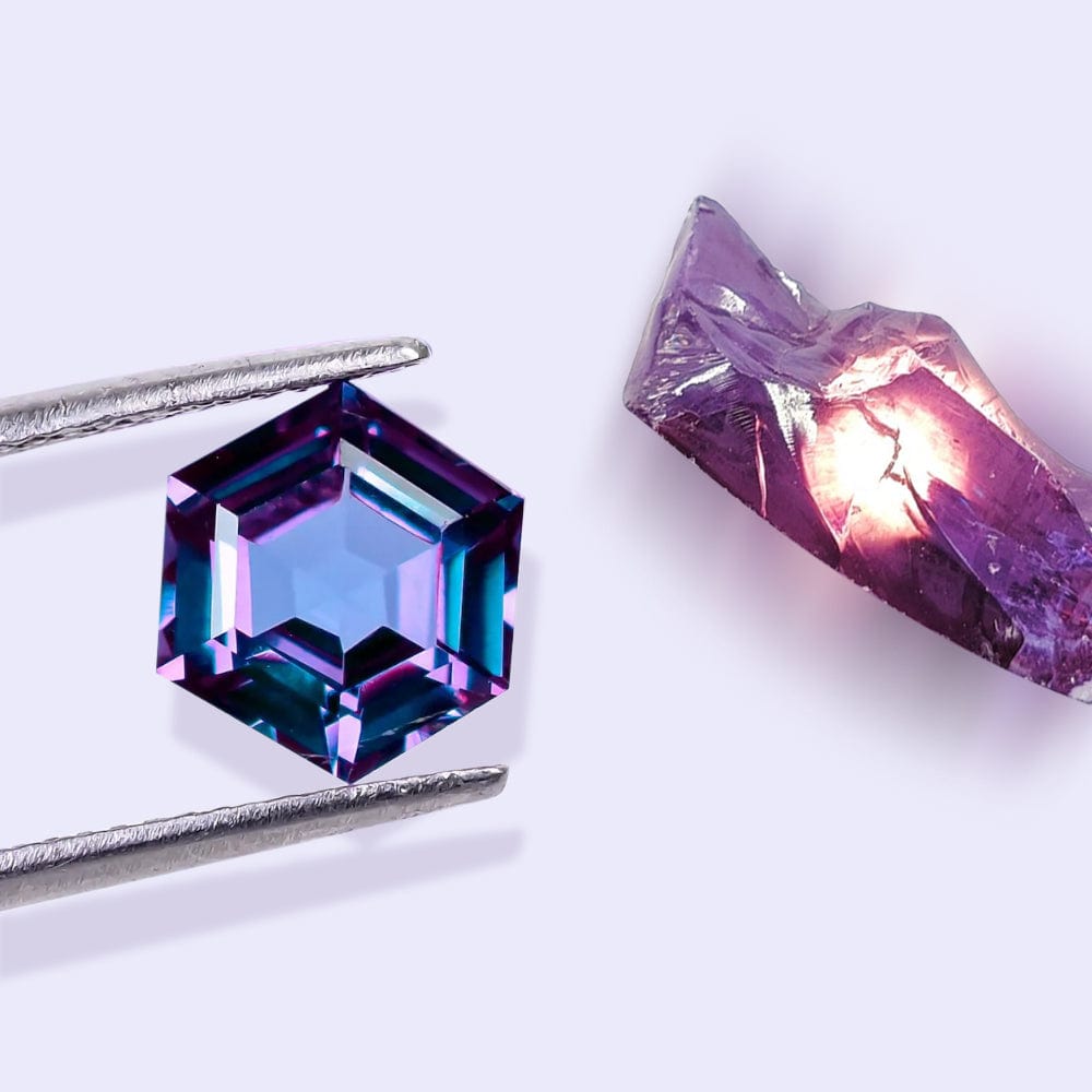 Hexagonal alexandrite gemstone with a rough crystal next to it on a white background