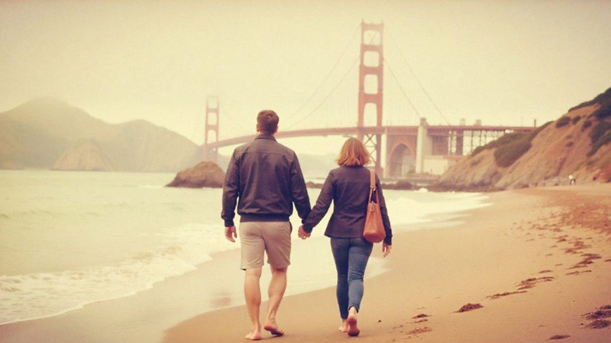 Two people walking on a beach with the Golden Gate Bridge in the background